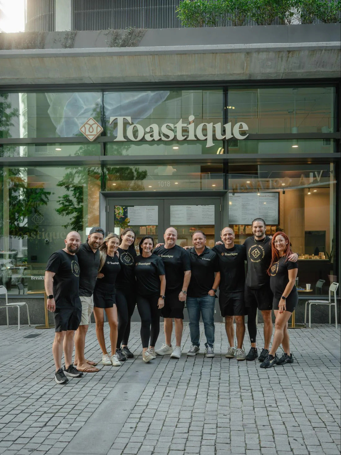 Toastique franchise team wearing branded shirts posing together outside a Toastique cafe storefront