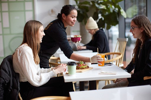 Team member serves fresh avocado toast, smoothie bowls, and cold-pressed juice to guests enjoying breakfast at Toastique Addison — the best breakfast in Addison, TX.