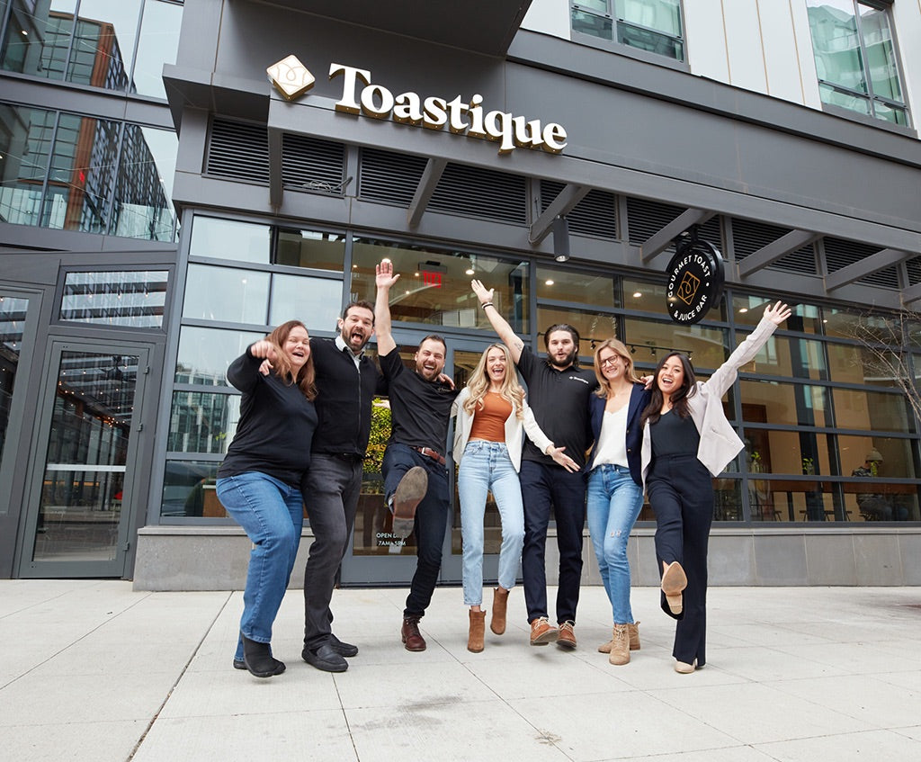 Toastique franchise owners celebrating outside a modern Toastique smoothie franchise storefront, showcasing one of the best smoothie franchise opportunities.