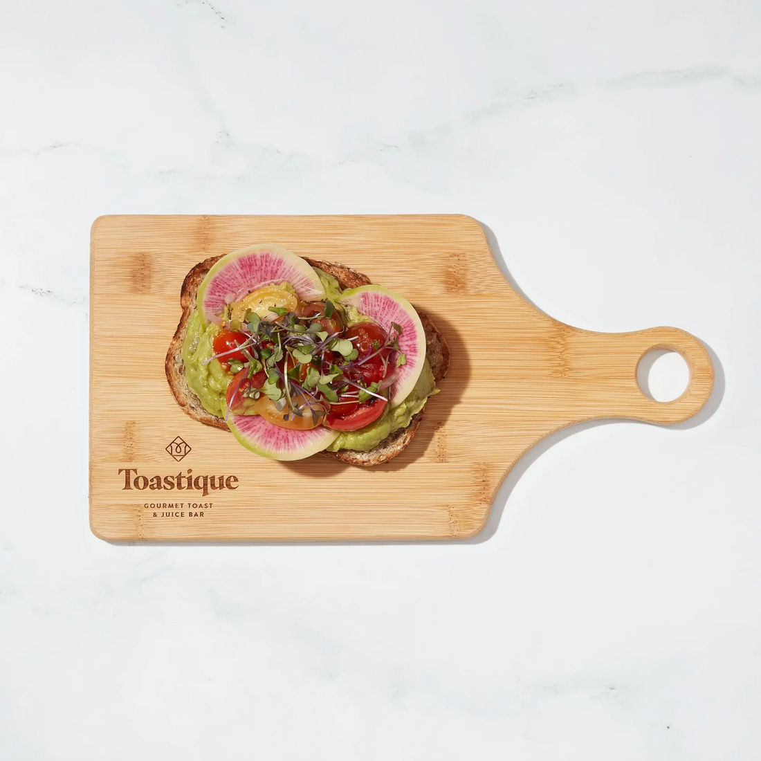 Avocado Smash toast recipe on wooden board at Toastique Vienna, VA, featuring fresh avocado, watermelon radish, marinated tomatoes, and microgreens on multigrain toast.