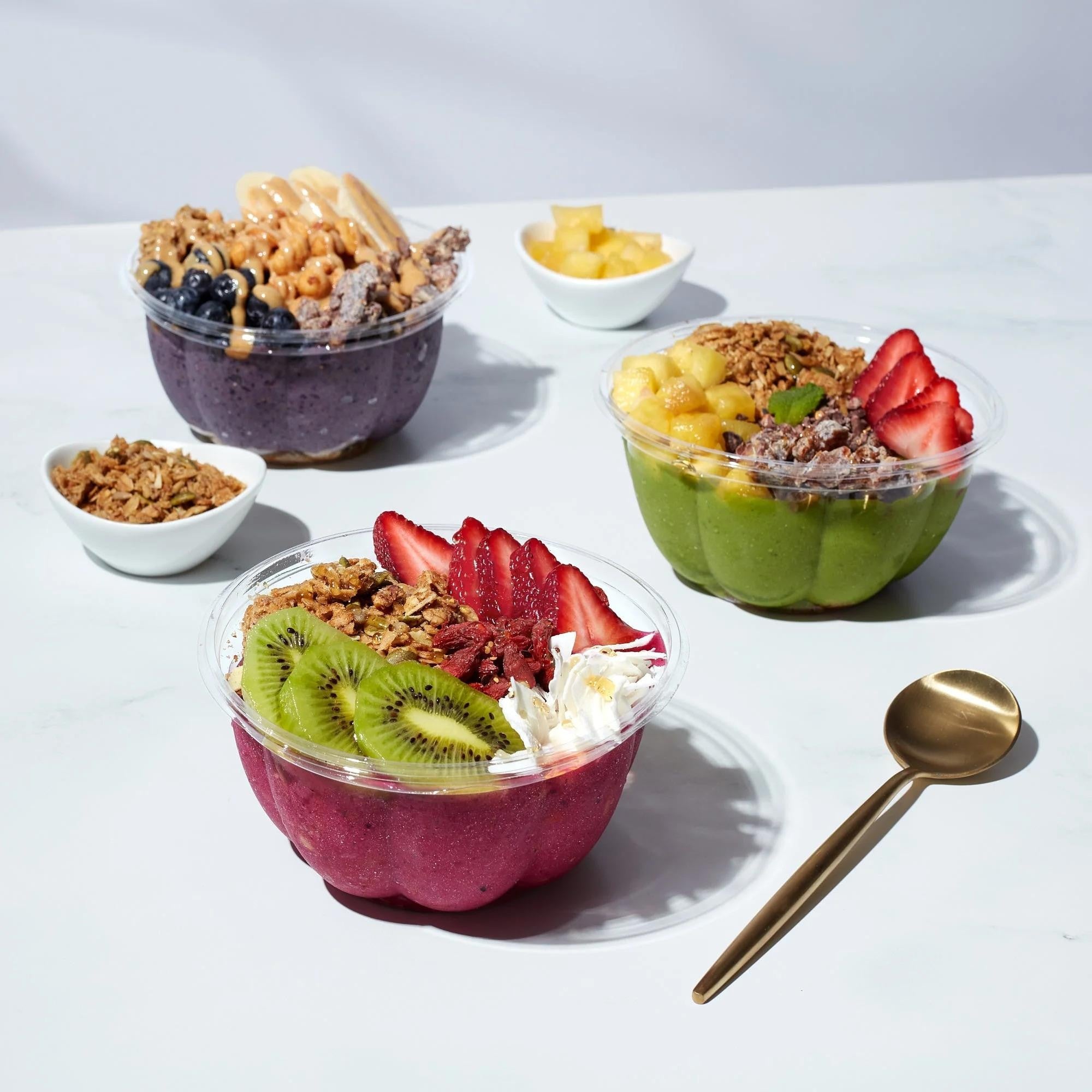 Three healthy smoothie bowls from Toastique featuring acai, matcha, and pitaya bases topped with fresh fruit, granola, and coconut