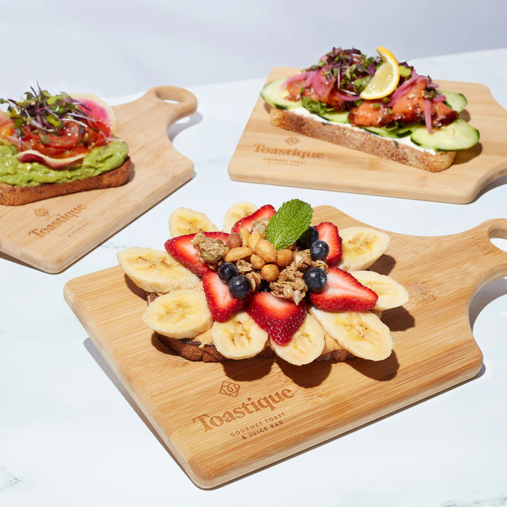 Toastique artisan toasts arranged on wooden boards with avocado toast, PB Crunch toast, and smoked salmon toast, perfect for food lovers searching for gourmet toast ideas.