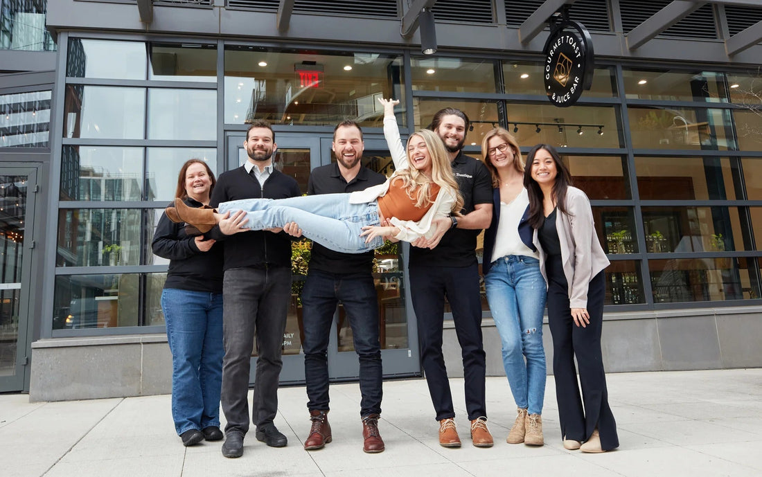 Toastique founder Brianna Keefe being lifted outside a Toastique café, celebrating teamwork, shared success, and the brand’s uplifting community culture.