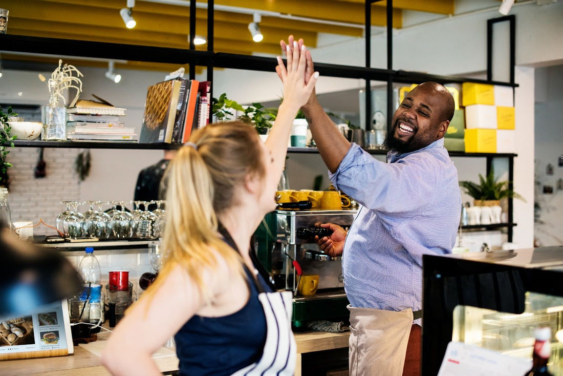 Two café franchise owners celebrating success with a high-five behind the counter of their modern café franchise concept.
