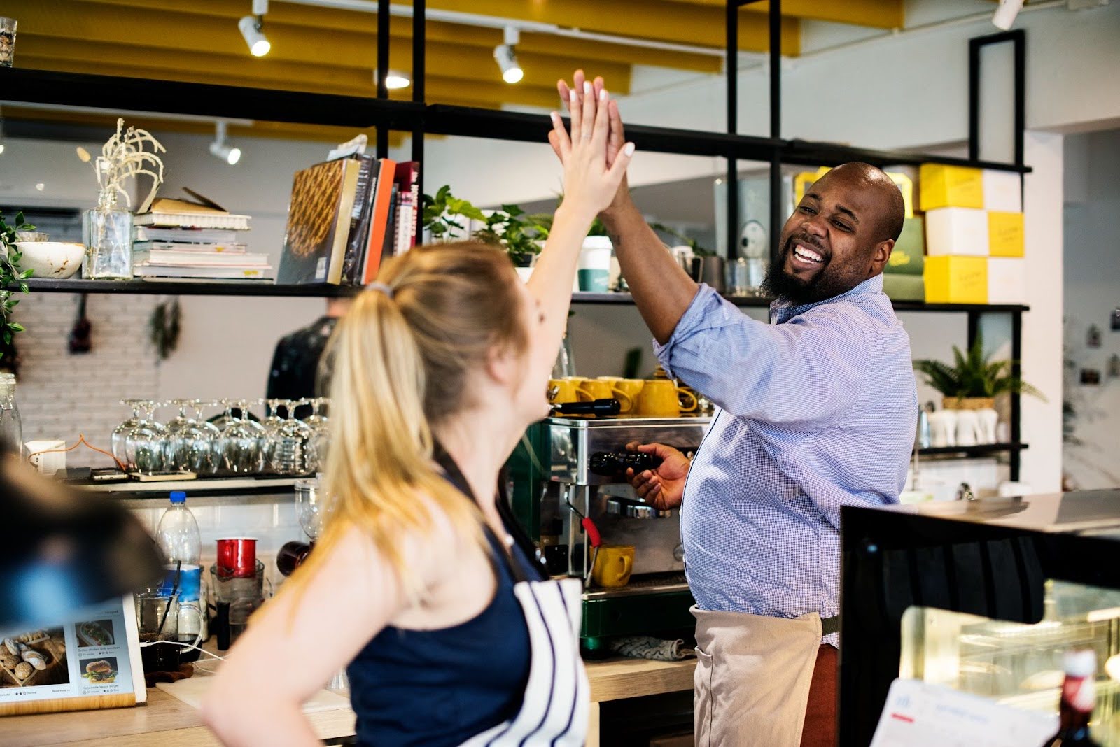 Two café franchise owners celebrating success with a high-five behind the counter of their modern café franchise concept.