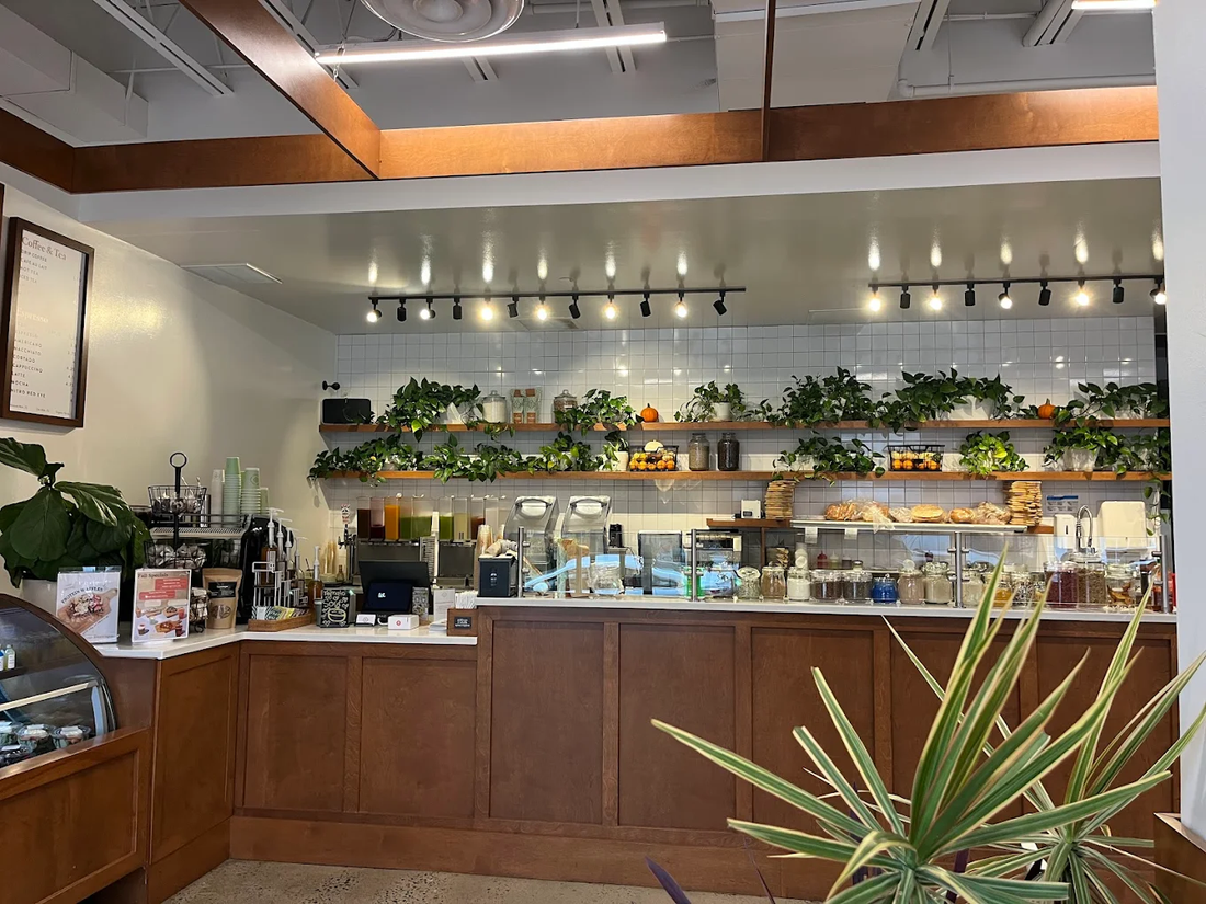 Bright and modern Toastique coffee shop interior in Alexandria, VA featuring white tables, wooden chairs, fresh ingredients on display, and warm wood accents.