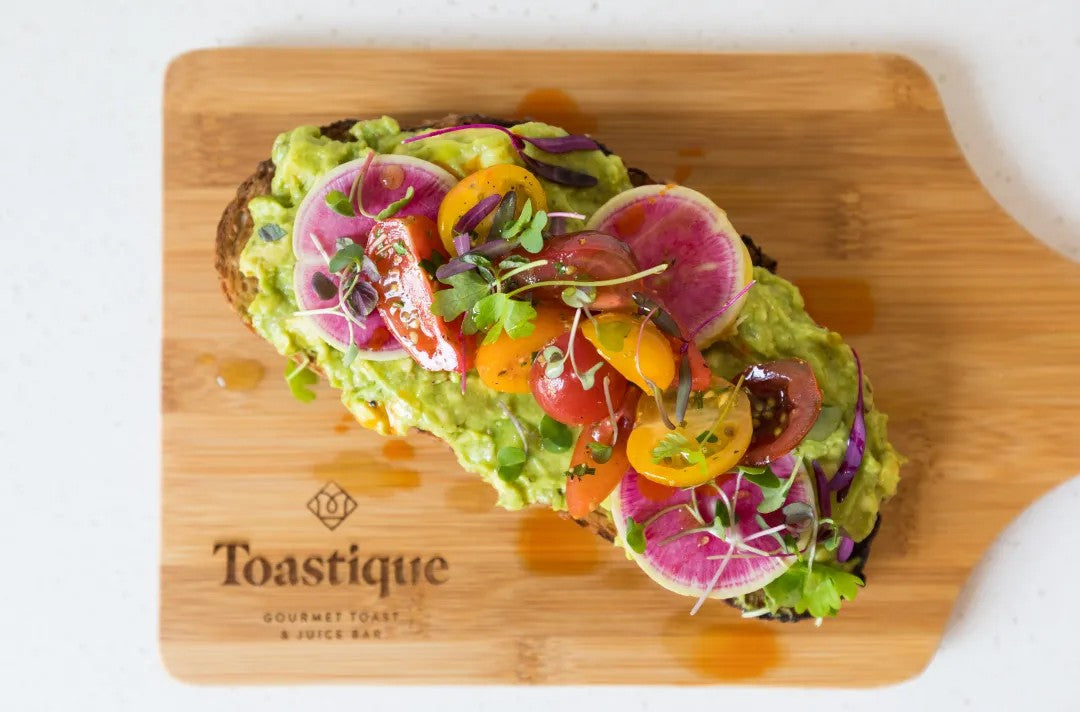 Gourmet avocado toast topped with heirloom tomatoes, watermelon radish, and microgreens at Toastique café franchise — a vibrant example of modern café franchise concepts.