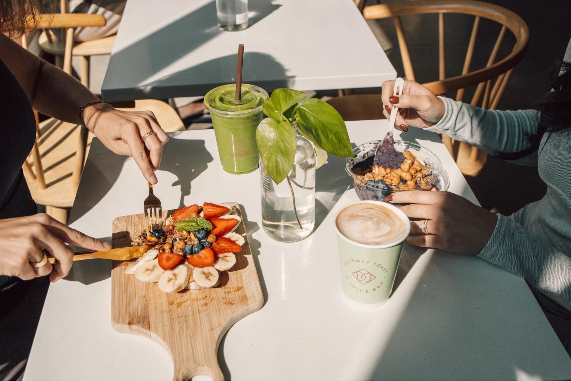 Guests enjoying avocado toast, smoothie, and latte inside a Toastique coffee bar franchise, showcasing fresh flavors and vibrant café dining.