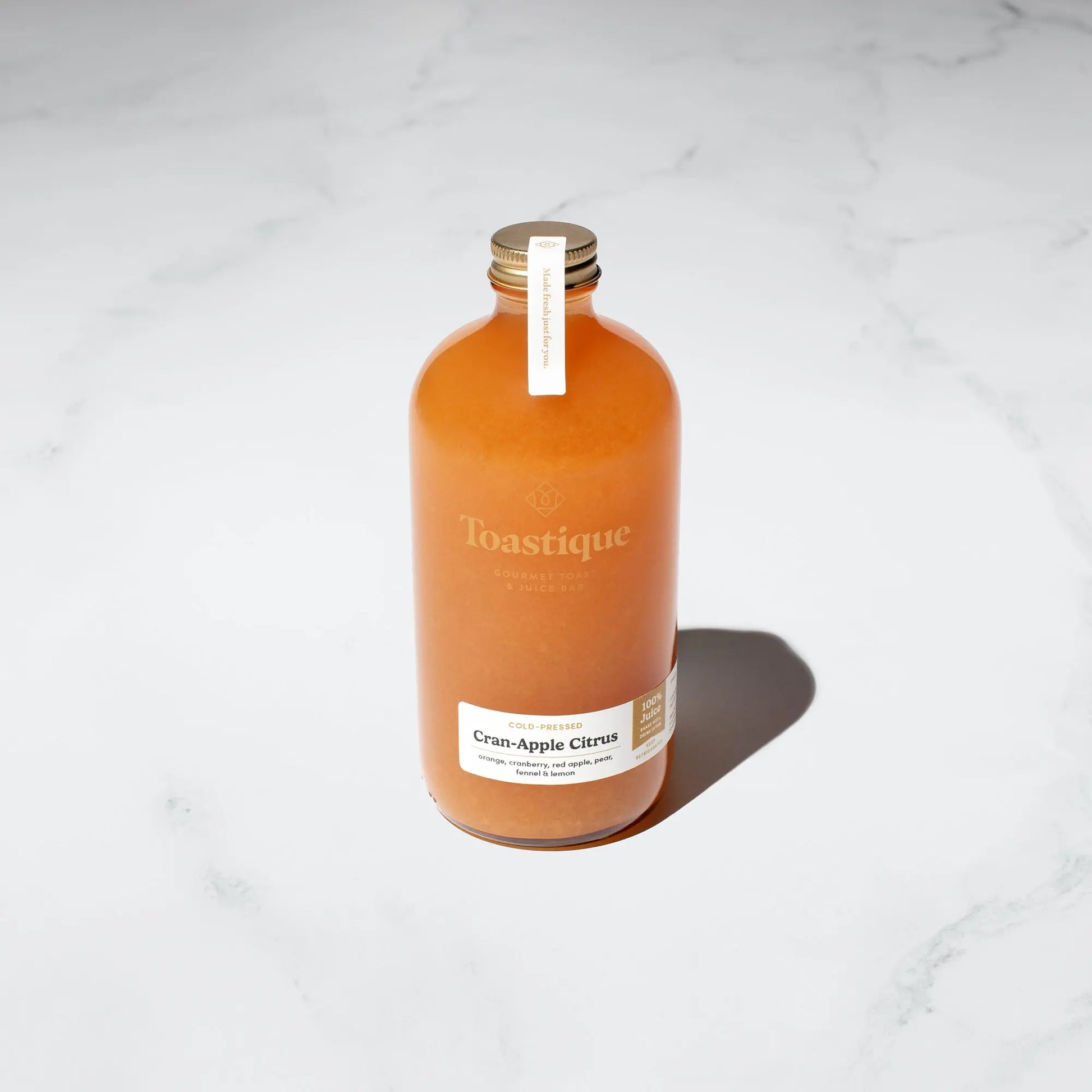 A glass bottle of Toastique Cran-Apple Citrus Cold-Pressed Juice.