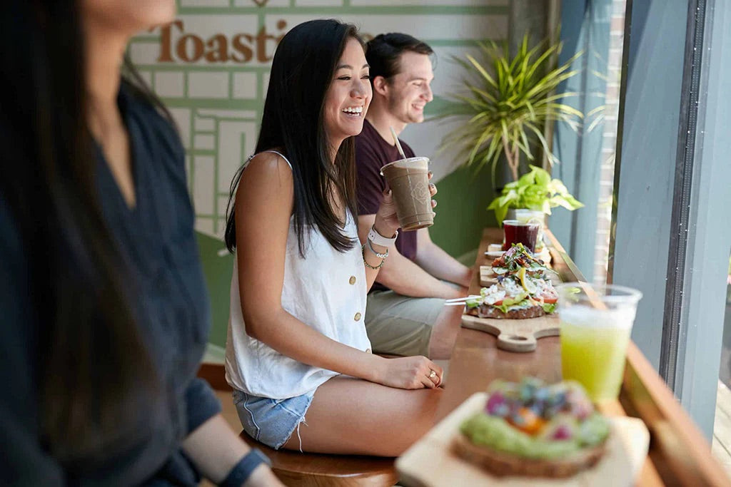 Guests enjoying smoothie drinks and colorful toasts inside a Toastique healthy food franchise, reflecting the energy of the best healthy food franchises.
